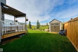 Spacious backyard featuring a wood deck with white railings, a covered patio area, a detached storage shed, and a wood fence - 
