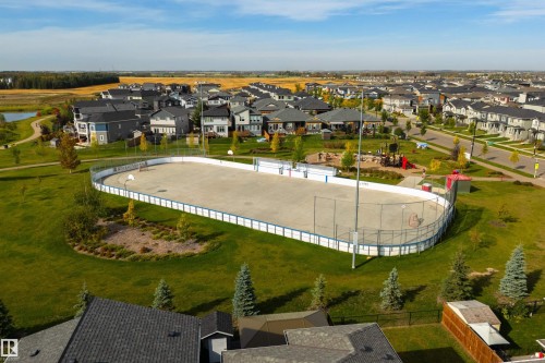 Outdoor rink with integrated basketball hoops, surrounded by green space, a playground, and residential properties - 1032 Berg Place, Leduc, AB 