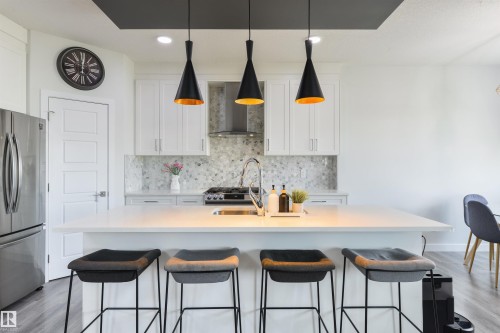 Kitchen featuring a large island with seating, white shaker-style cabinetry, mosaic tile backsplash, stainless steel appliances, and wood-finish flooring - 1032 Berg Place, Leduc, AB 