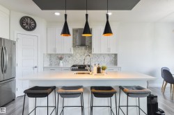 Kitchen featuring a large island with seating, white shaker-style cabinetry, mosaic tile backsplash, stainless steel appliances, and wood-finish flooring - 