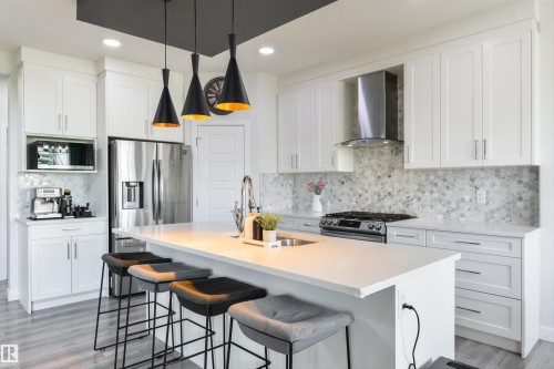 Modern kitchen featuring white cabinetry, a large center island with a sink, stainless steel appliances, and a unique tiled backsplash - 1032 Berg Place, Leduc, AB 