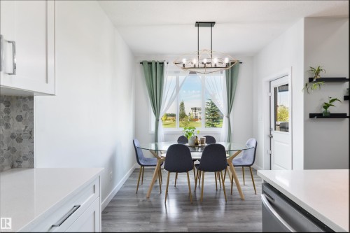 Open dining area with wood-finish flooring, a contemporary chandelier, and a large window - 1032 Berg Place, Leduc, AB 
