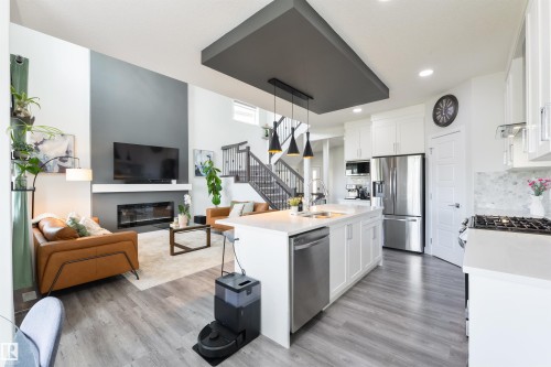 Open-concept living space with wood-finish flooring, a contemporary fireplace, and a kitchen island with built-in sink - 1032 Berg Place, Leduc, AB 