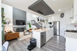 Open-concept living space with wood-finish flooring, a contemporary fireplace, and a kitchen island with built-in sink - 