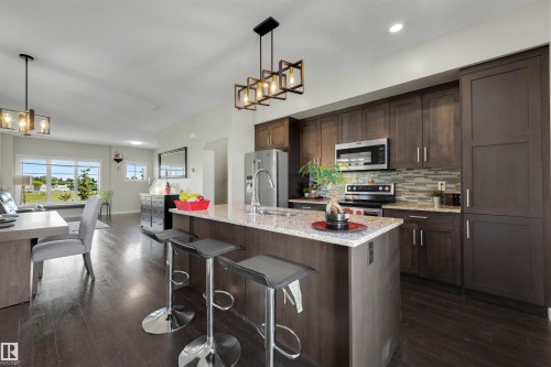 Contemporary kitchen featuring a center island with countertop seating, stainless steel appliances, dark wood-finish cabinetry, and a subway tile backsplash - #1 1636 Kerr Rd Nw, Edmonton, AB 
