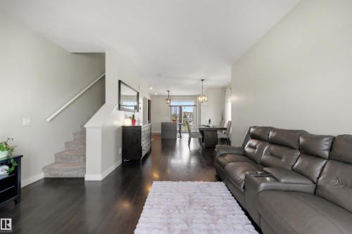 Open-concept living area featuring dark wood-finish flooring, light grey walls, and a carpeted staircase with a white handrail - #1 1636 Kerr Rd Nw, Edmonton, AB 