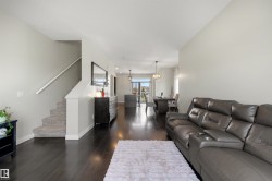 Open-concept living area featuring dark wood-finish flooring, light grey walls, and a carpeted staircase with a white handrail - 