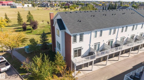 White siding exterior with a dark shingled roof, multiple balconies with white railings, and a brick-clad chimney - #1 1636 Kerr Rd Nw, Edmonton, AB 