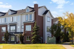 Multi-level townhouse exterior featuring brick and siding finishes, multiple dormer windows, and a prominent brick chimney - 