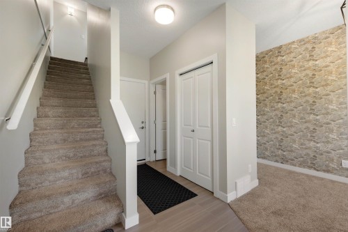 Carpeted staircase with white railings, natural stone accent wall, light wood-finish flooring, and a white bi-fold closet - #1 1636 Kerr Rd Nw, Edmonton, AB 