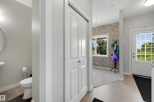 Powder room with a pedestal sink and round mirror, stone accent wall, dual-pane windows, and a glass-paneled entry door - #1 1636 Kerr Rd Nw, Edmonton, AB 