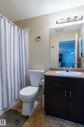 Bathroom featuring a dark wood-finish vanity with a single basin sink, light-toned countertop, and a contemporary four-bulb vanity light fixture - #214 1188 Hyndman Rd Nw, Edmonton, AB 
