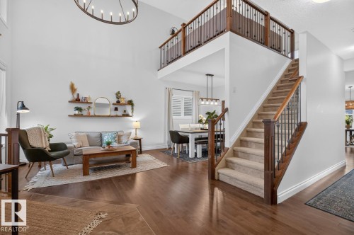 Soaring ceiling with a large chandelier, wood-finish flooring, staircase with wood banister and wrought iron spindles, open concept dining area, and upper-level railing overlooking the living space - 21 Altadena Point(E), Sherwood Park, AB 