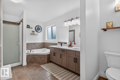 Dual vanity with integrated sinks, large soaking tub, glass-enclosed shower, tile flooring, and a large window - 21 Altadena Point(E), Sherwood Park, AB 