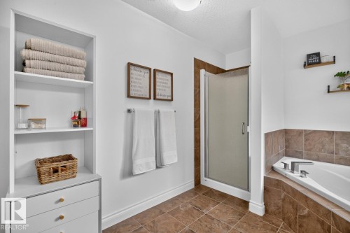 White built-in shelving with drawers, a separate shower enclosure with frosted glass, a corner soaking tub, and brown tiled flooring - 21 Altadena Point(E), Sherwood Park, AB 