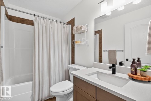 Integrated white tub and shower unit, brown tile shower surround, single vanity with light-toned countertop, matte black faucet, and wood-finish cabinetry - 21 Altadena Point(E), Sherwood Park, AB 