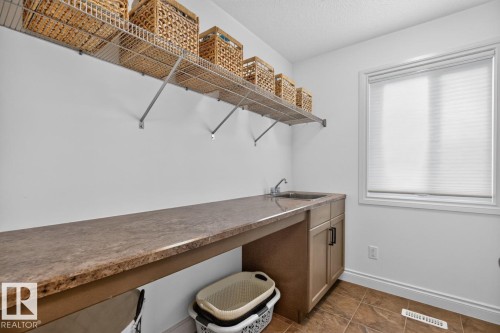 White walls with a window, brown tiled flooring, and a long countertop with a built-in sink - 21 Altadena Point(E), Sherwood Park, AB 
