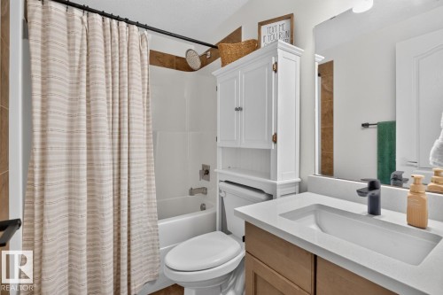 Bathroom featuring a white bathtub, tiled shower surround, wood-finish vanity with an integrated sink, black faucet, and a large wall mirror - 21 Altadena Point(E), Sherwood Park, AB 