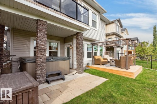 Ground-level patio with a hot tub, stone-clad support columns, and an elevated wood deck featuring a pergola - 21 Altadena Point(E), Sherwood Park, AB 
