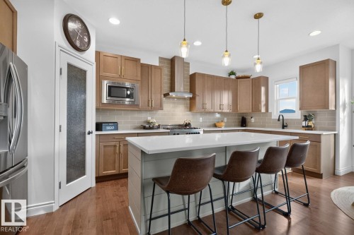 Stainless steel refrigerator, wood-finish flooring, light-toned cabinetry, light subway tile backsplash, and a center island with seating - 21 Altadena Point(E), Sherwood Park, AB 