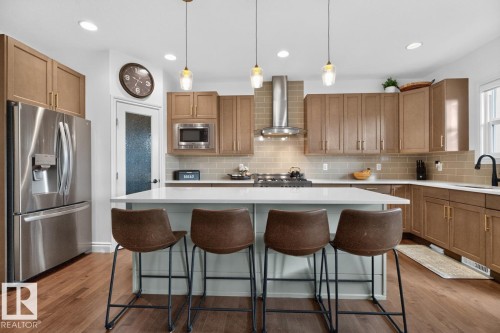Stainless steel appliances, wood-finish flooring, light wood cabinetry, white countertop island, and subway tile backsplash - 21 Altadena Point(E), Sherwood Park, AB 