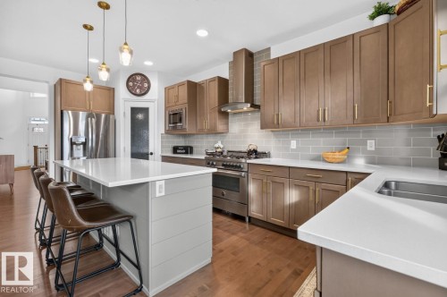 Kitchen featuring a center island with white countertop, stainless steel appliances, wood-finish cabinetry, and a tile backsplash - 21 Altadena Point(E), Sherwood Park, AB 
