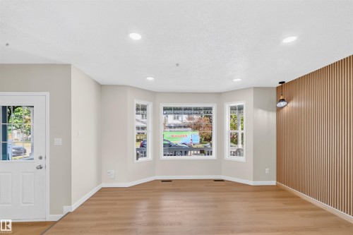Light wood-finish flooring, recessed ceiling lighting, a decorative slatted wall feature, and a prominent bay window - 4409 150 Avenue Nw, Edmonton, AB 