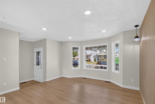 Wood-finish flooring throughout, recessed ceiling lighting, bay window, front entry door with glass panels, and a wood-slat accent wall - 4409 150 Avenue Nw, Edmonton, AB 