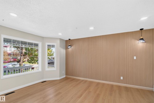 Wood-finish flooring throughout, bay windows with white framing, recessed lighting, and an accent wall featuring vertical wood paneling - 4409 150 Avenue Nw, Edmonton, AB 