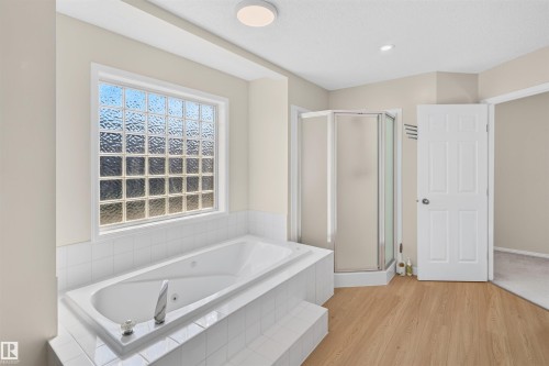 Soaking tub with tiled surround, glass block window, corner shower enclosure, and wood-finish flooring - 4409 150 Avenue Nw, Edmonton, AB 