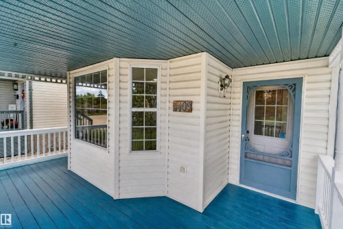 Covered porch with a blue-painted floor and ceiling, white railing, and exterior wall paneling - 4409 150 Avenue Nw, Edmonton, AB 