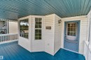 Covered porch with a blue-painted floor and ceiling, white railing, and exterior wall paneling - 4409 150 Avenue Nw, Edmonton, AB 