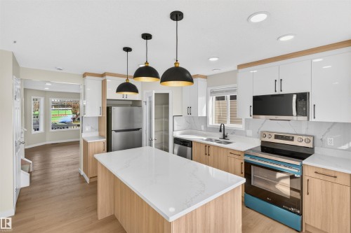 Modern kitchen featuring wood-finish lower cabinetry, white upper cabinetry, and a center island with a light-toned countertop - 4409 150 Avenue Nw, Edmonton, AB 
