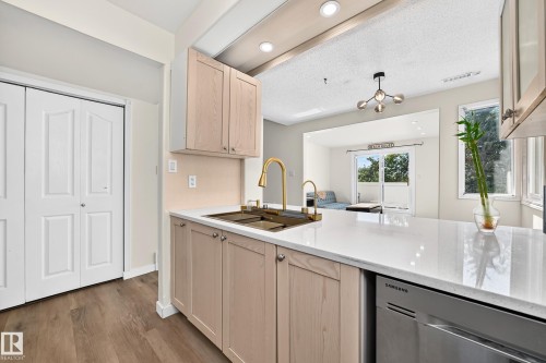 Contemporary kitchen featuring warm wood-finish cabinetry, white quartz countertops, a center island with seating space, stainless steel appliances, and a brass pull-down faucet - 161 Lancaster Terrace Nw, Edmonton, AB 