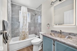 Bathroom featuring a window, gray wall tiling, wood-finish flooring, a vanity with a counter and an undermount sink, and an illuminated mirror - 