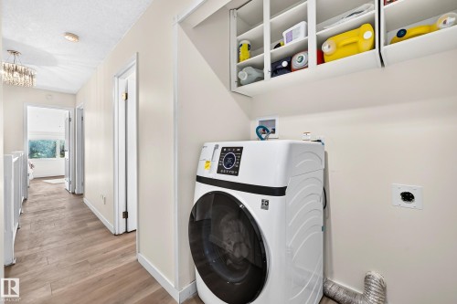Hallway laundry area featuring a front-load appliance, integrated wall cabinetry, and wood-finish flooring - 161 Lancaster Terrace Nw, Edmonton, AB 