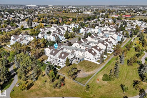 White multi-level townhouse complex with gabled roofs, surrounded by mature trees and paved pathways - 161 Lancaster Terrace Nw, Edmonton, AB 