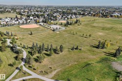 Expansive green space featuring recreational fields, mature trees, paved walking paths, and a distant residential backdrop - 