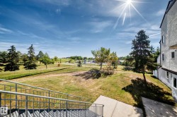 Exterior building with multiple windows, metal staircase with handrails, concrete landing, and a grassy expanse with mature trees - 