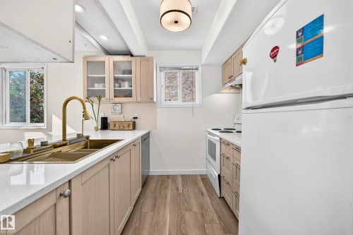 Kitchen featuring light wood-finish cabinetry, white countertops, dual-basin sink with gold-tone faucet, wood-finish flooring, and a white range - 161 Lancaster Terrace Nw, Edmonton, AB 