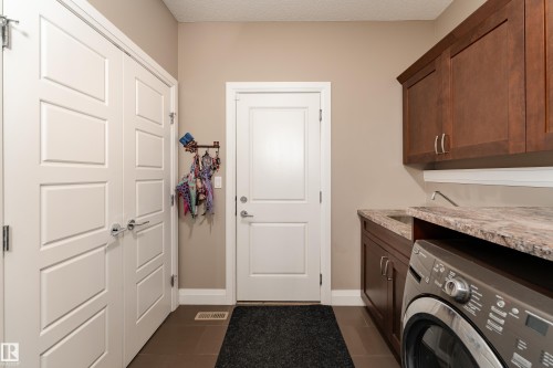 Laundry area featuring wood-finish cabinetry, a built-in sink, and stone-look countertops - 6613 31 Avenue, Beaumont, AB 