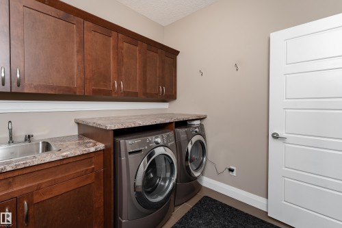 Wood-finish cabinetry with brushed nickel hardware, stainless steel sink with coordinating faucet, and stone-finish countertops - 6613 31 Avenue, Beaumont, AB 
