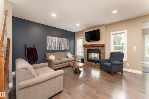 Living area featuring a stone-clad fireplace with wood mantle, wood-finish flooring, recessed lighting, and multiple windows - 6613 31 Avenue, Beaumont, AB 