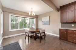 Hardwood-finish flooring, recessed wood cabinetry, L-shaped countertop, window with white trim, and a multi-light chandelier - 