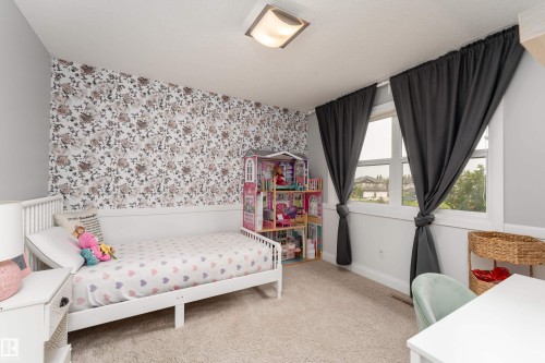 Neutral wall color with a floral accent wall, window with dark drapes, and plush carpet flooring - 6613 31 Avenue, Beaumont, AB 