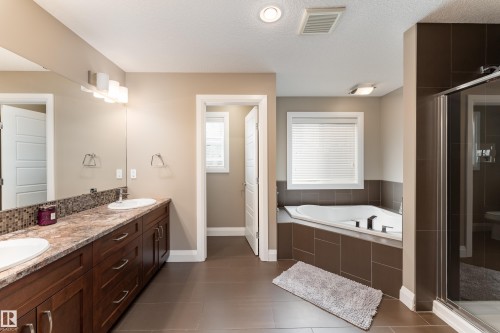 Dual vanity with integrated sinks, mosaic tile backsplash, built-in corner tub, and a glass-enclosed shower - 6613 31 Avenue, Beaumont, AB 