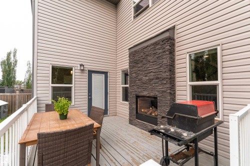 Spacious outdoor deck featuring light-colored siding, a dark stone-clad fireplace with a built-in firebox, and a glass-paneled exterior door - 6613 31 Avenue, Beaumont, AB 
