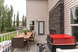 Outdoor deck with a white railing, wood-finish decking, and an exterior fireplace featuring stacked stone - 