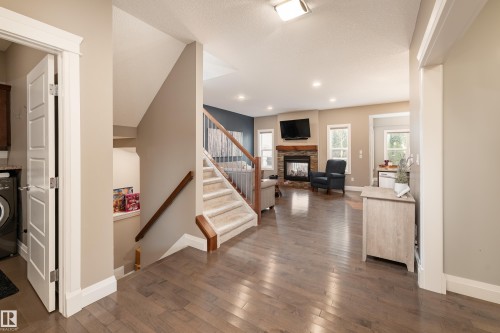 Wood-finish flooring throughout, carpeted staircase with wood handrails, recessed lighting, stone-faced fireplace with wood mantel, and multiple windows providing natural light - 6613 31 Avenue, Beaumont, AB 