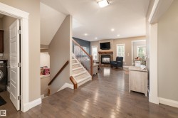 Wood-finish flooring throughout, carpeted staircase with wood handrails, recessed lighting, stone-faced fireplace with wood mantel, and multiple windows providing natural light - 
